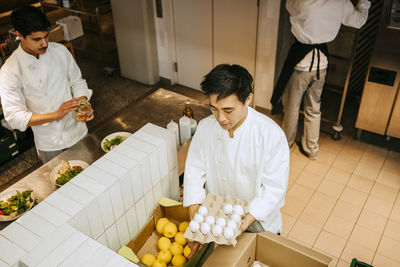 High angle view of male chef with egg crate in hand standing at commercial kitchen