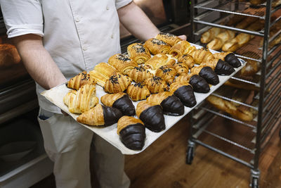 Male chef holding baking sheet filled with croissant in bakery kitchen