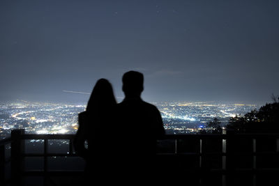 Rear view of silhouette couple against illuminated city at night