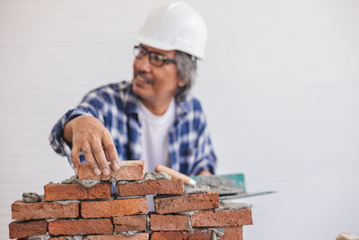 Mature man wearing hardhat making brick wall in workshop