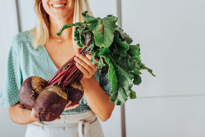 Young woman midsection holding beetroots with green leaves and smiling