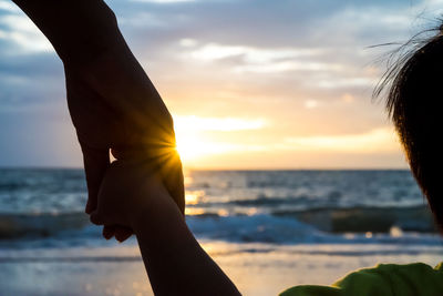 Cropped image of parent holding child hand against sky during sunset