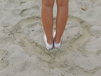 Low section of woman standing on sand at beach