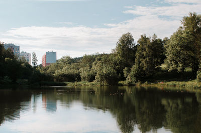 Scenic view of lake by trees and buildings against sky