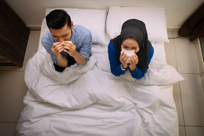 Woman holding umbrella while sitting on bed at home