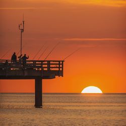 Rear view of silhouette men on pier fishing in sea at sunset