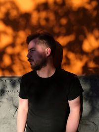 Young man looking away while standing against wall