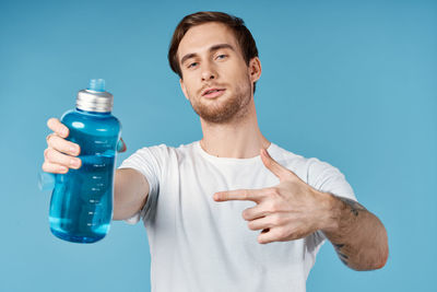 Young man holding bottle against blue background