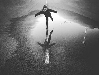 Girl standing with arms outstretched on water puddle