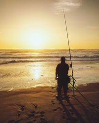 Person fishing in sea against sky during sunset