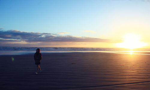 Full length of woman walking at beach against sky during sunset