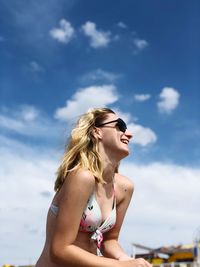 Cheerful young woman wearing sunglasses and bikini top against sky during summer