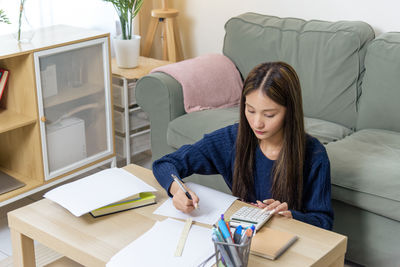 Young woman using digital tablet while sitting on sofa at home