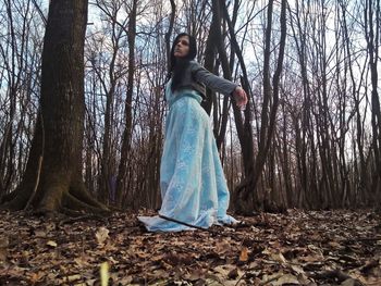 Young woman standing by tree trunk in forest