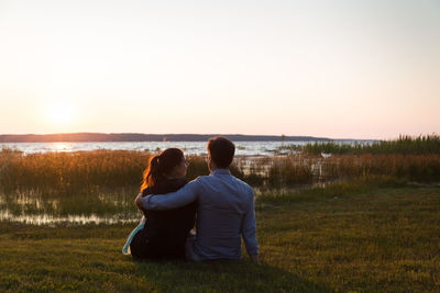 Rear view of couple sitting on field against sky during sunset