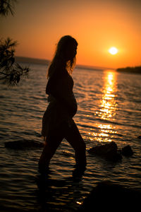 Silhouette woman by sea against sky during sunset