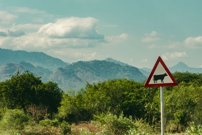 Road sign by trees against landscape and sky