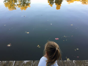 Rear view of girl sitting on pier over lake