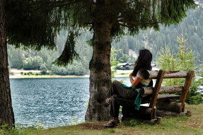 Woman sitting on bench against lake