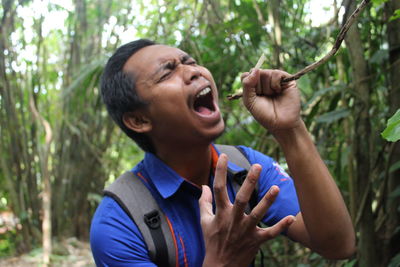 Young man screaming while holding twig in forest