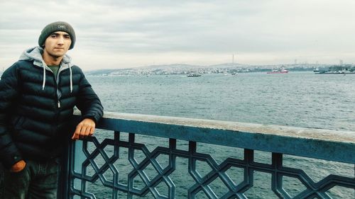 Portrait of young man standing by railing against sea