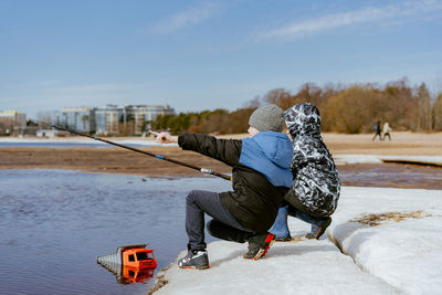 Cute little caucasian boys pretending fishing looking into distance on sea side on spring day