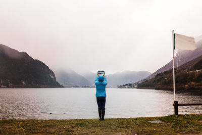 Rear view of woman standing by lake against clear sky