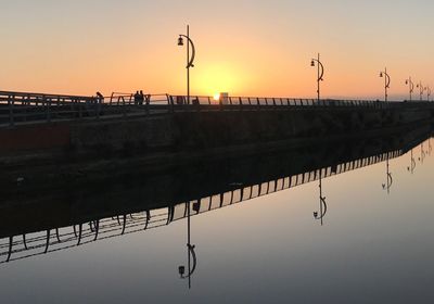 Silhouette bridge over lake against sky during sunset