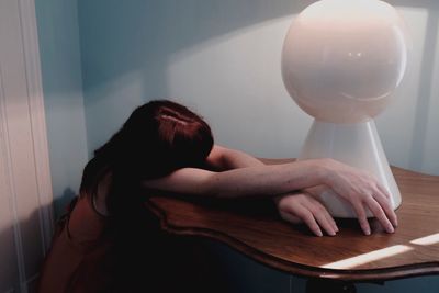 Mid adult woman lying on wooden table against wall at home