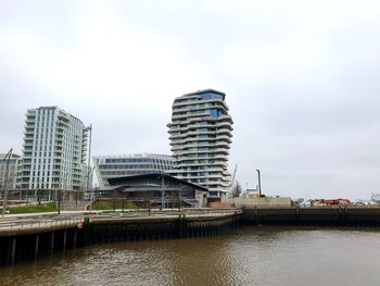 Modern buildings by river against sky in city