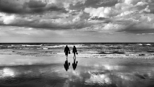 Rear view of man and woman walking beach against cloudy sky