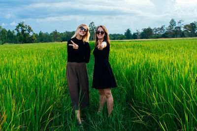 Portrait of smiling women embracing while standing on field against sky