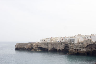 Buildings on cliff by sea at polignano a mare against sky