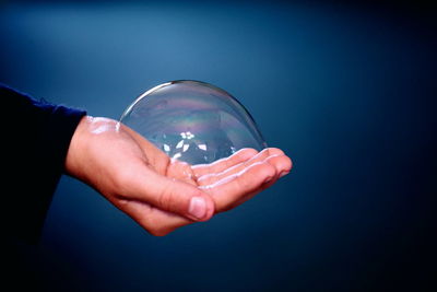 Cropped hand holding bubble against blue background