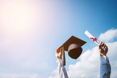 Low angle view of man holding graduation cap