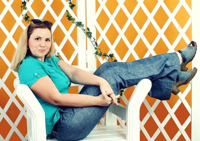 Portrait of mid adult woman sitting with feet up on chair against white fence