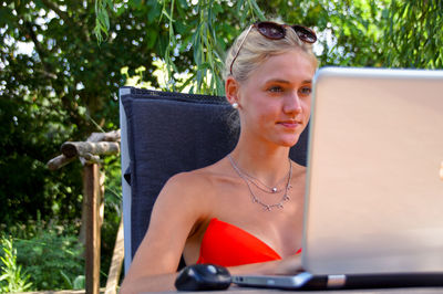 Young woman using laptop while sitting against plants in yard