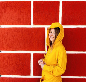 Full length of a smiling young woman standing against red wall