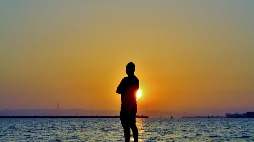 Rear view of silhouette man standing by sea against sky during sunset