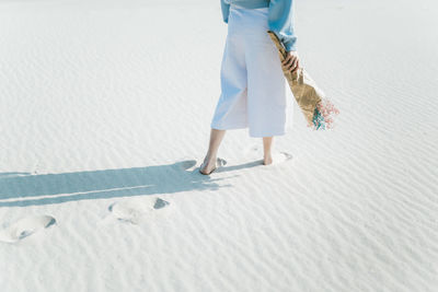 Low section of woman holding flower bouquet while walking at sandy beach