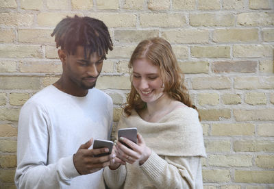 Young man using mobile phone against brick wall