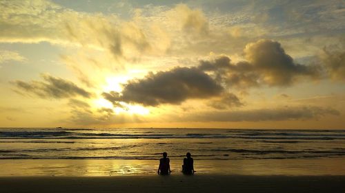 Silhouette people on beach against sky during sunset