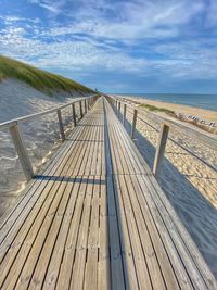 Boardwalk leading towards sea against sky