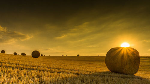 Hay bales on field against sky during sunset