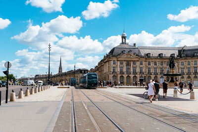 People walking on street amidst buildings in city against sky