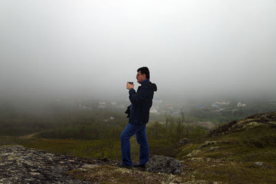 Full length of man photographing on mobile phone in fog