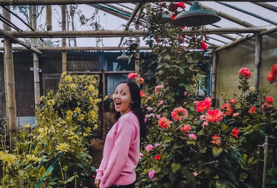 Portrait of smiling woman standing by flowering plants