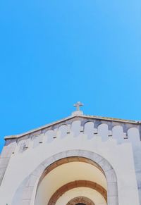 Low angle view of cross on building against clear blue sky