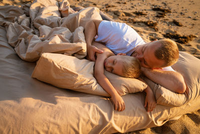 Family vacation in summer on sandy beach. father and son are lying on an air mattress on bed linen.