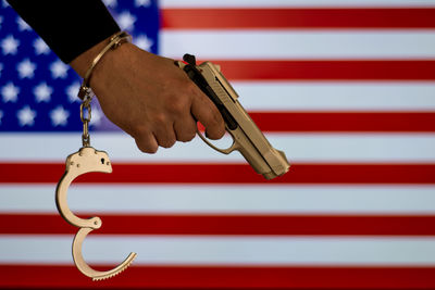 Cropped hand of male criminal holding gun against american flag